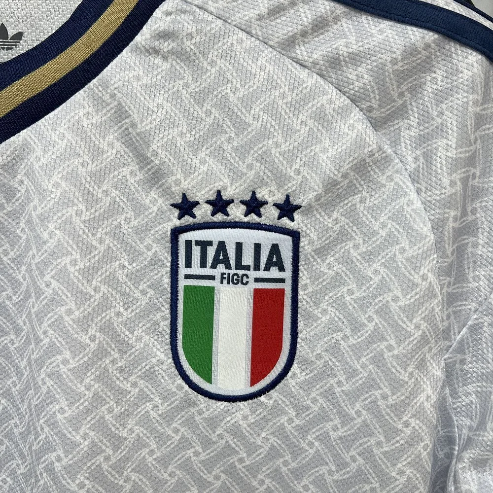 Primer plano del escudo de la selección italiana de fútbol bordado sobre fondo blanco con texturas geométricas.
