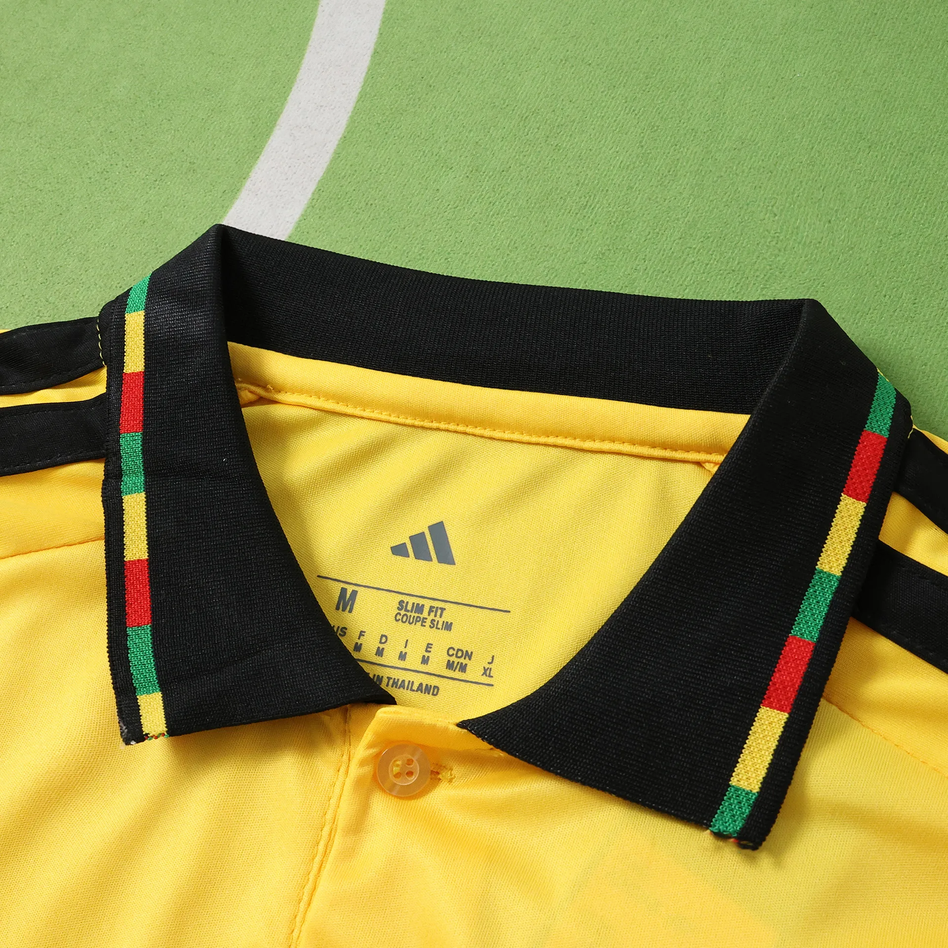 Detalle del cuello tipo polo en color negro con botones y ribete tricolor de la selección de Jamaica.