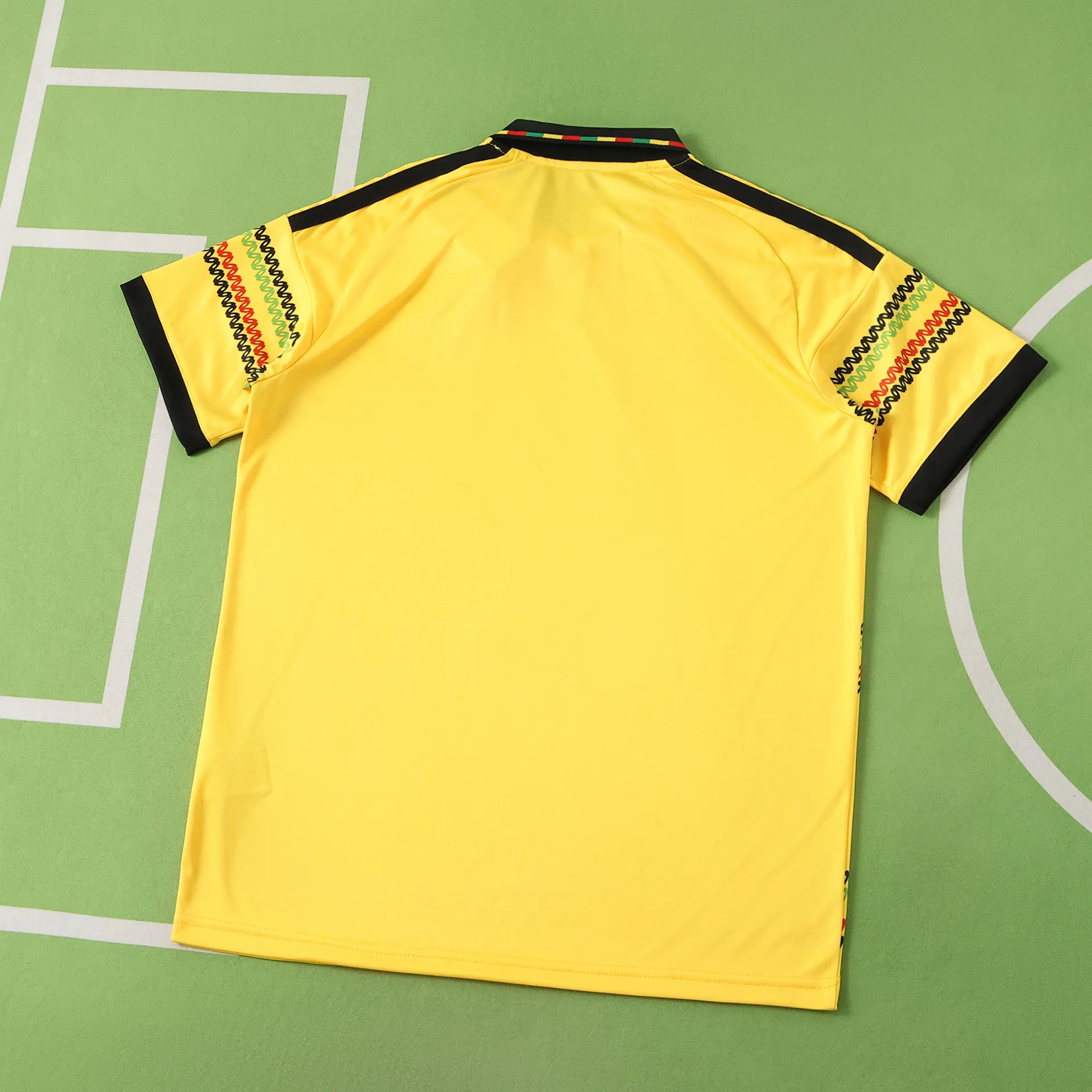 Vista posterior de la equipación de Jamaica en color amarillo liso con detalle tricolor en el borde del cuello.