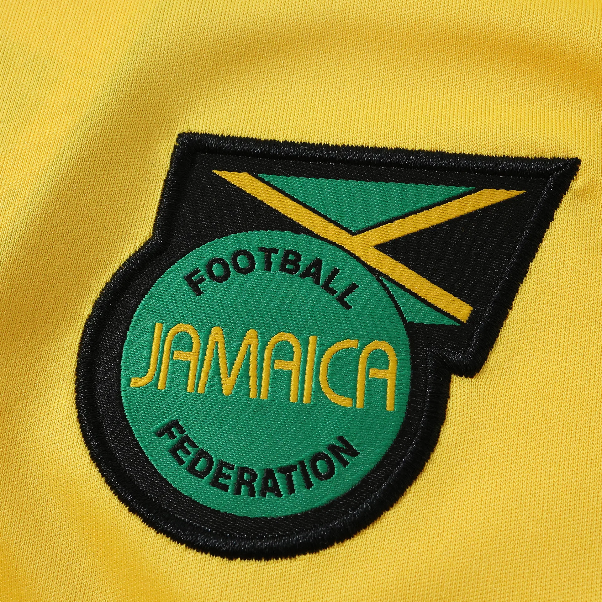 Primer plano del escudo de la Federación de Fútbol de Jamaica bordado sobre fondo amarillo.