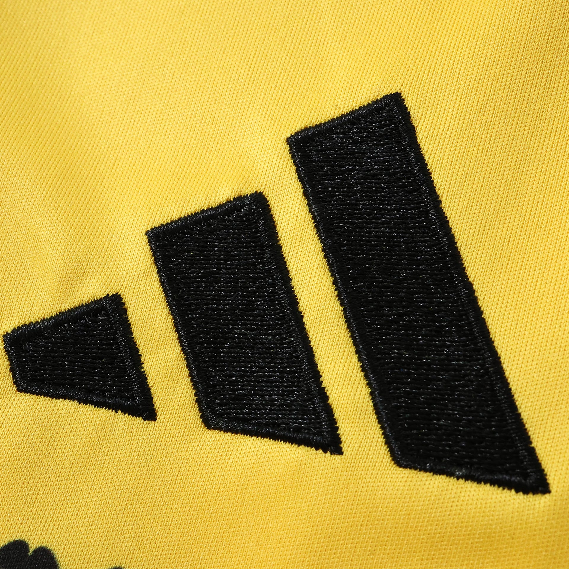 Detalle del bordado decorativo en color negro sobre el tejido técnico amarillo de la prenda.