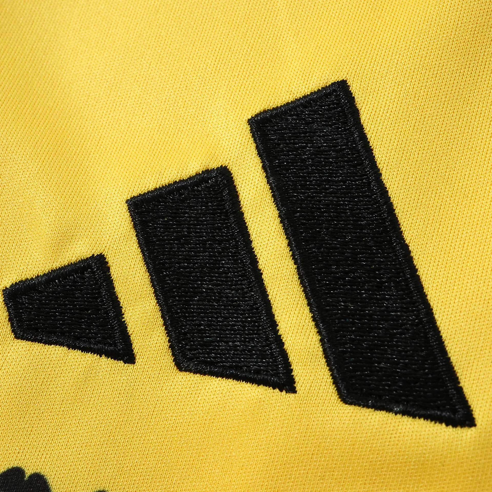 Detalle del bordado decorativo en color negro sobre el tejido técnico amarillo de la prenda.
