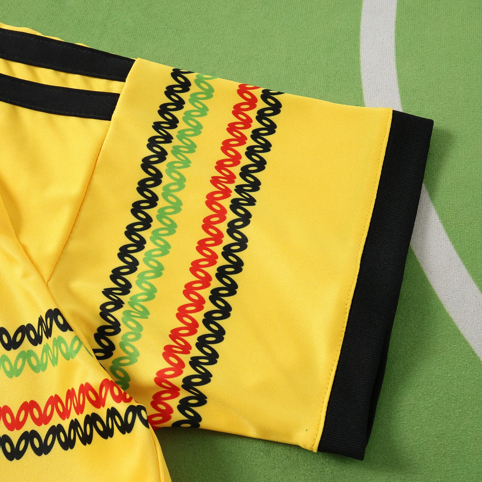 Detalle de la manga amarilla con un patrón bordado de ondas en colores negro, verde y rojo, representativos de Jamaica.