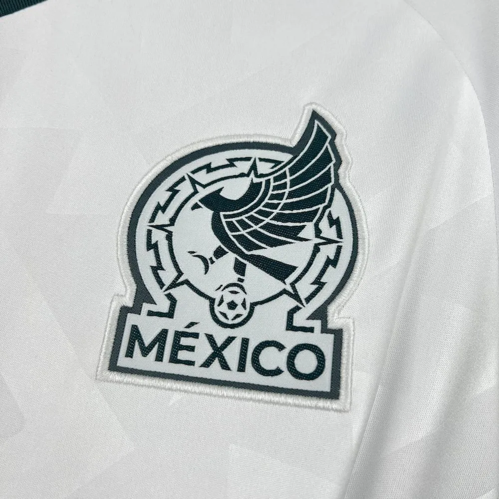 Primer plano del escudo de la selección de México bordado en verde oscuro sobre el diseño de la tela visitante.