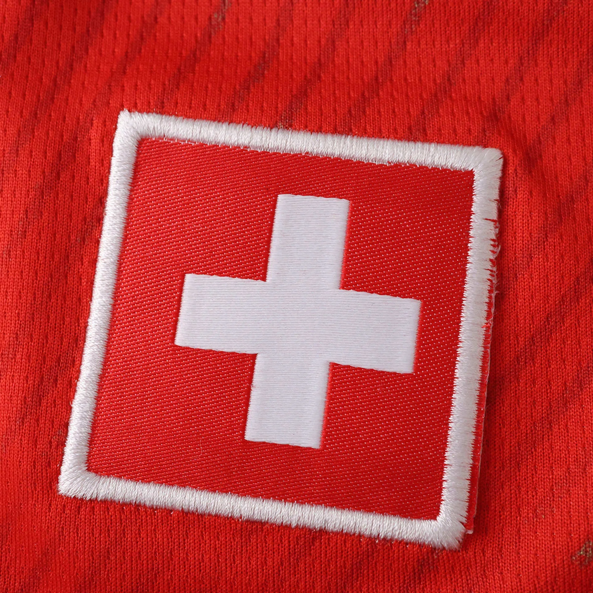 Detalle del escudo nacional de Suiza con la cruz blanca sobre fondo rojo cuadrado bordado en la camiseta.