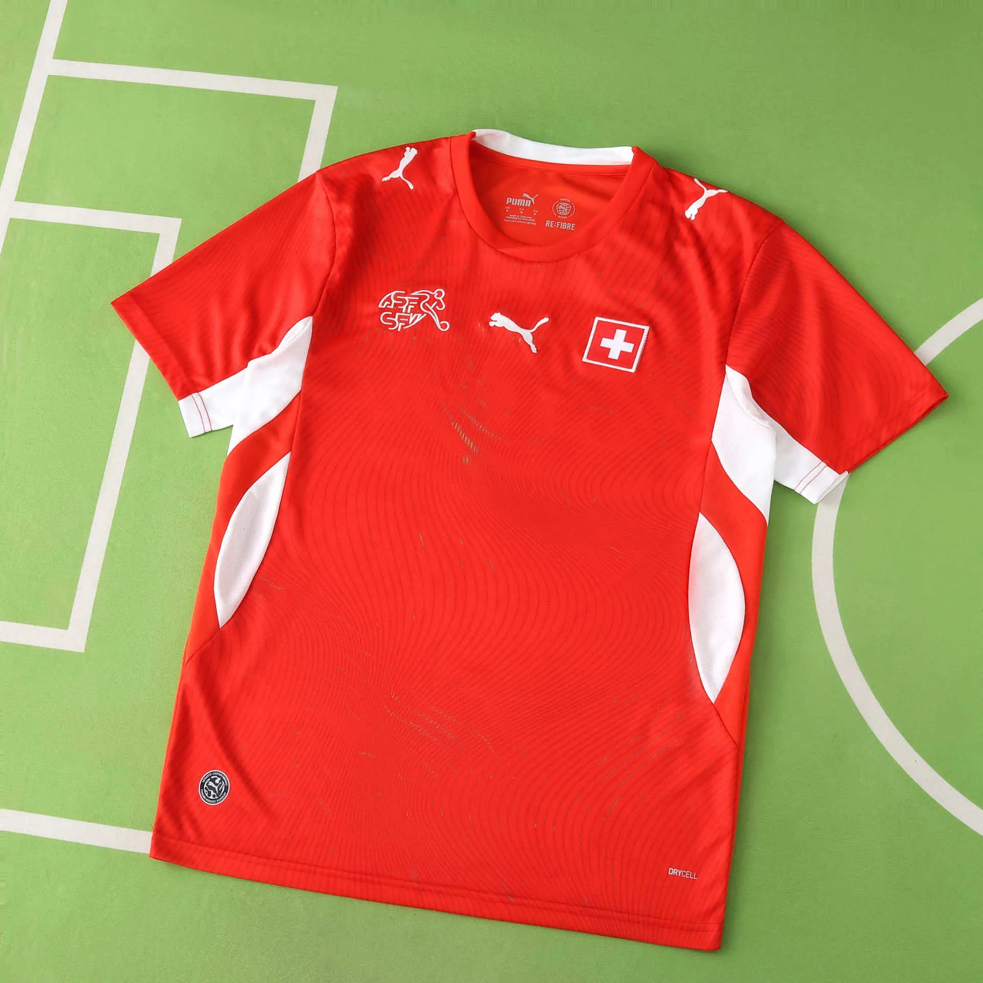 Vista frontal completa de la camiseta de Suiza para el Mundial 2026, color rojo con paneles laterales blancos y patrón de líneas finas.