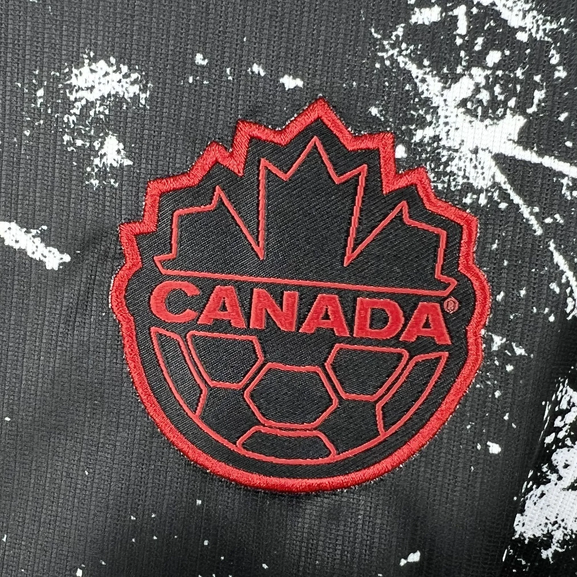 Detalle del escudo de la selección de Canadá con la hoja de maple sobre el círculo, bordado en rojo sobre el tejido blanco.
