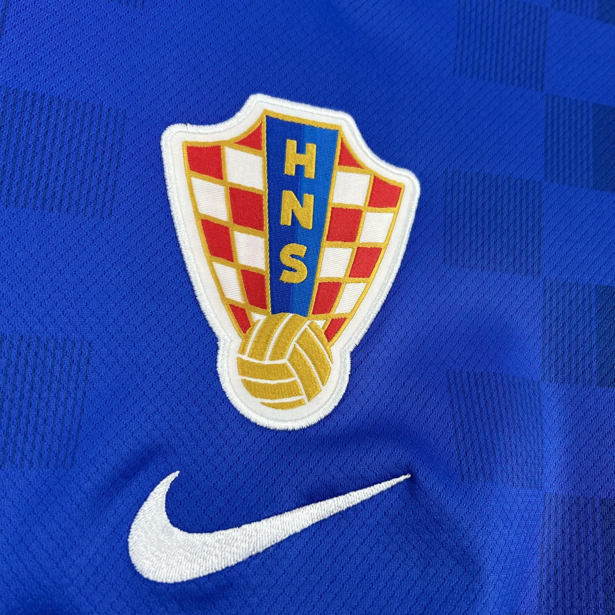 Detalle del escudo de la federación croata bordado sobre el patrón de damero azul de la camiseta.