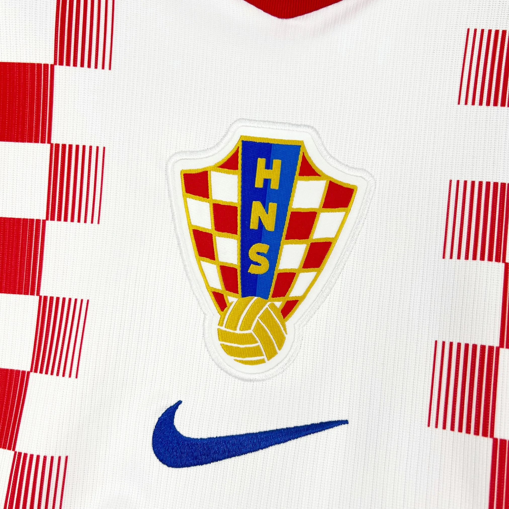 Primer plano del escudo de la Federación Croata de Fútbol con el diseño de cuadros, un balón dorado y las siglas "HNS" en azul.
