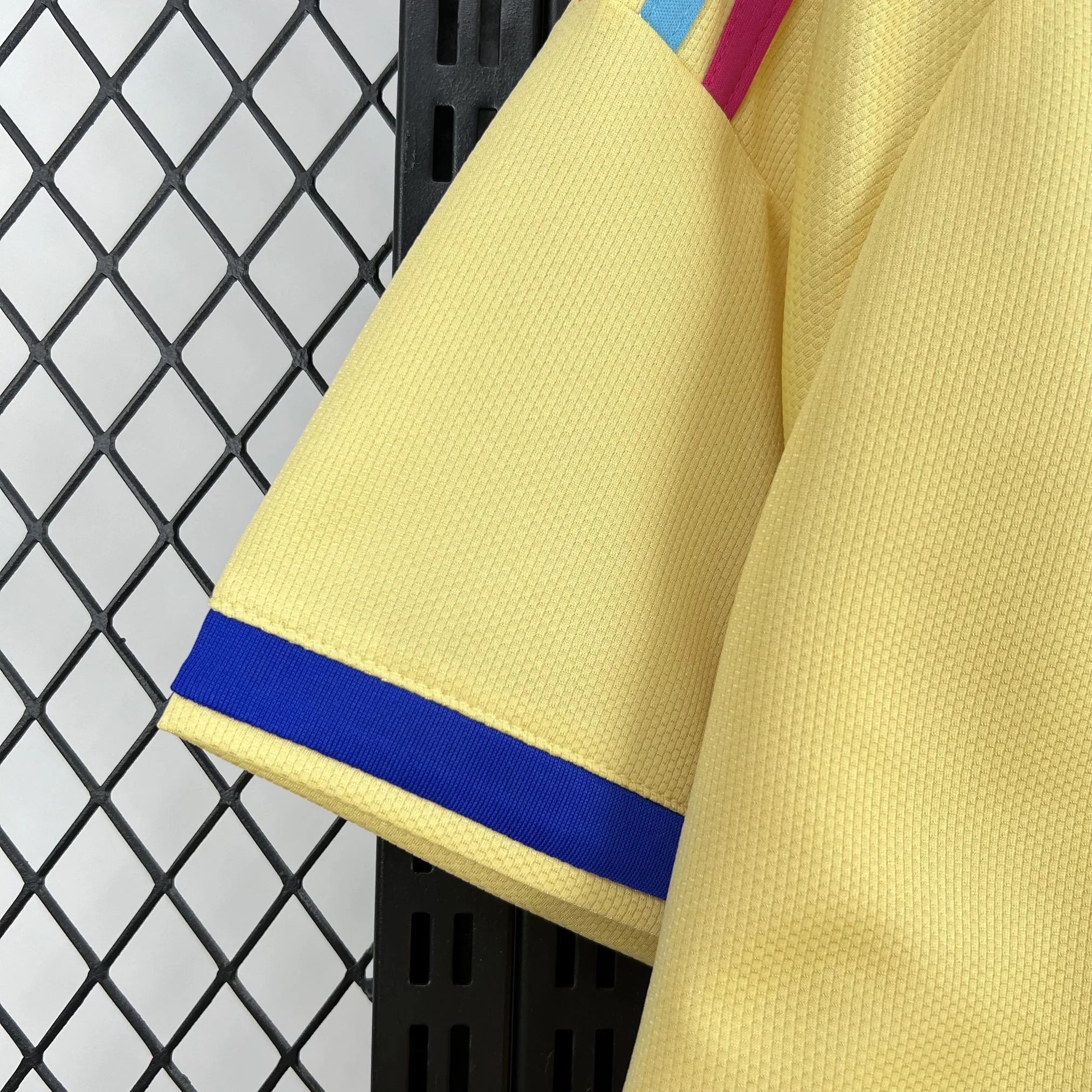 Detalle de la manga blanca destacando el puño elástico bicolor en amarillo y azul, y sutiles gráficos culturales.