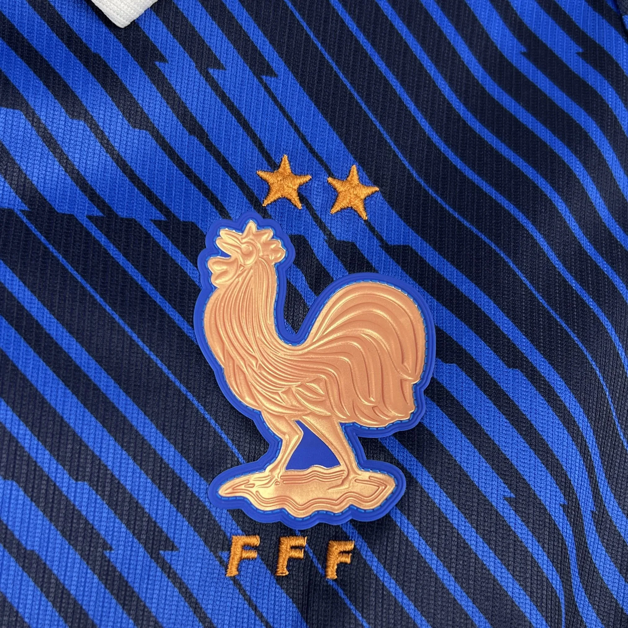 Detalle del escudo de la selección francesa con el gallo dorado de gran tamaño bordado sobre el tejido azul.