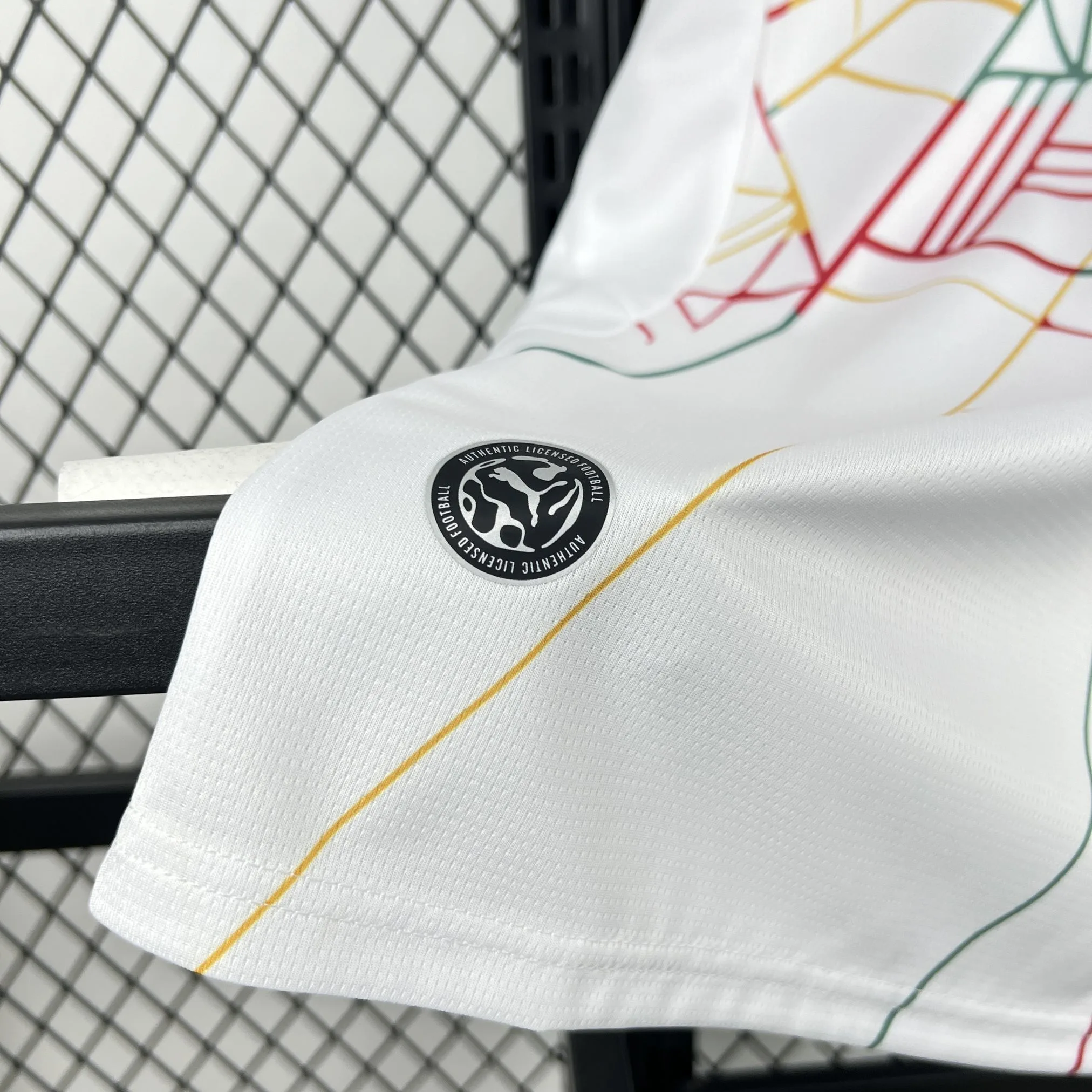 Detalle del borde inferior de la equipación de Ghana mostrando el tejido técnico blanco y el sello circular de autenticidad.