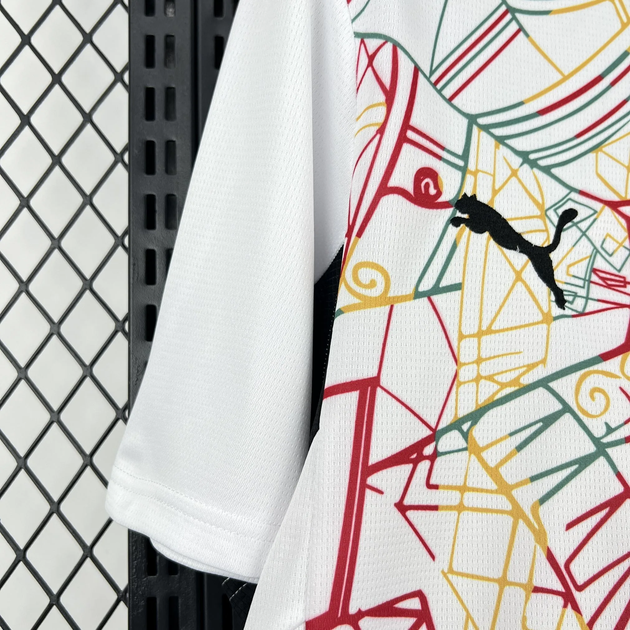 Detalle de la manga blanca y el patrón artístico lineal en colores verde, amarillo y rojo de la camiseta de Ghana.