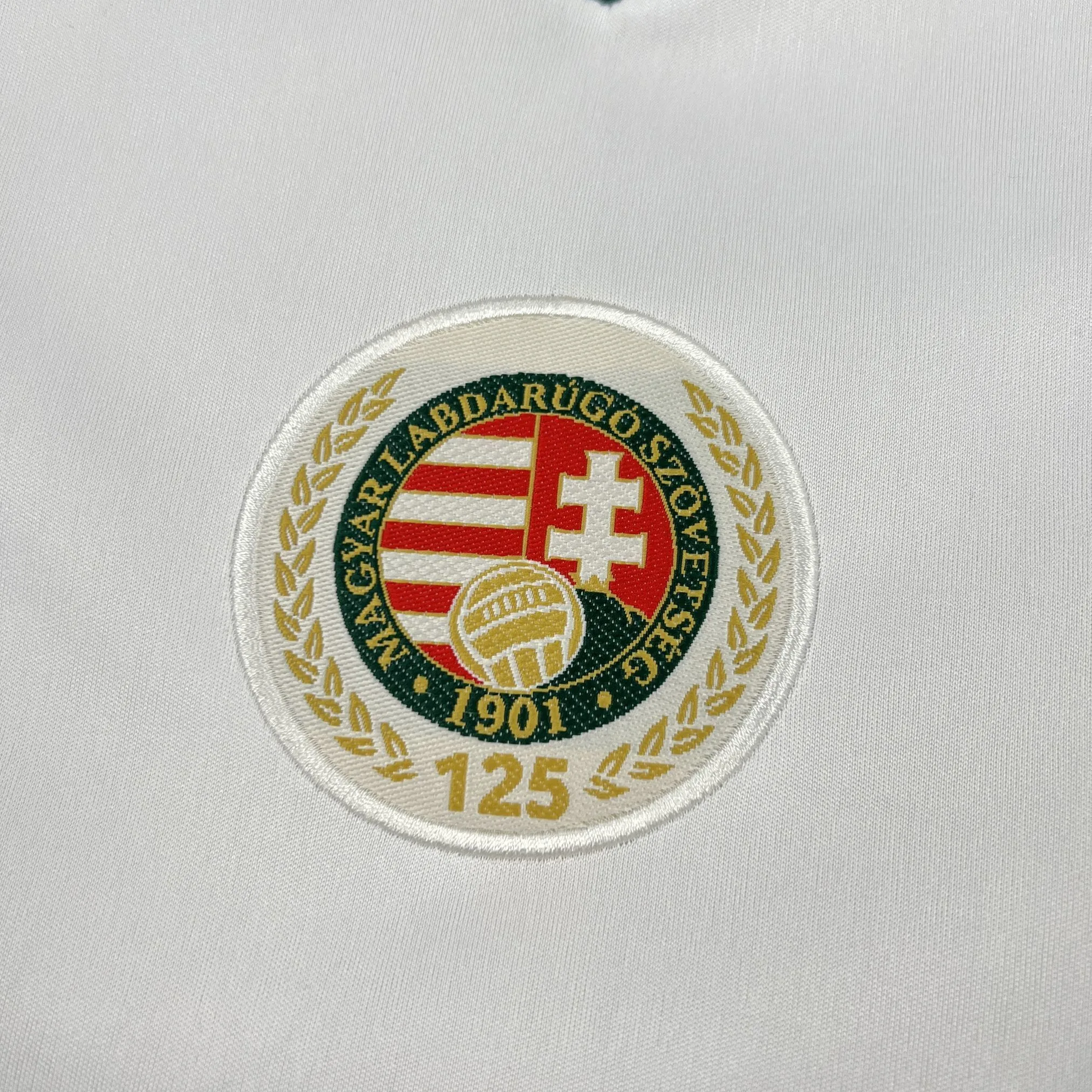 Primer plano del escudo de la Federación Húngara de Fútbol (MLSZ) bordado sobre fondo blanco.