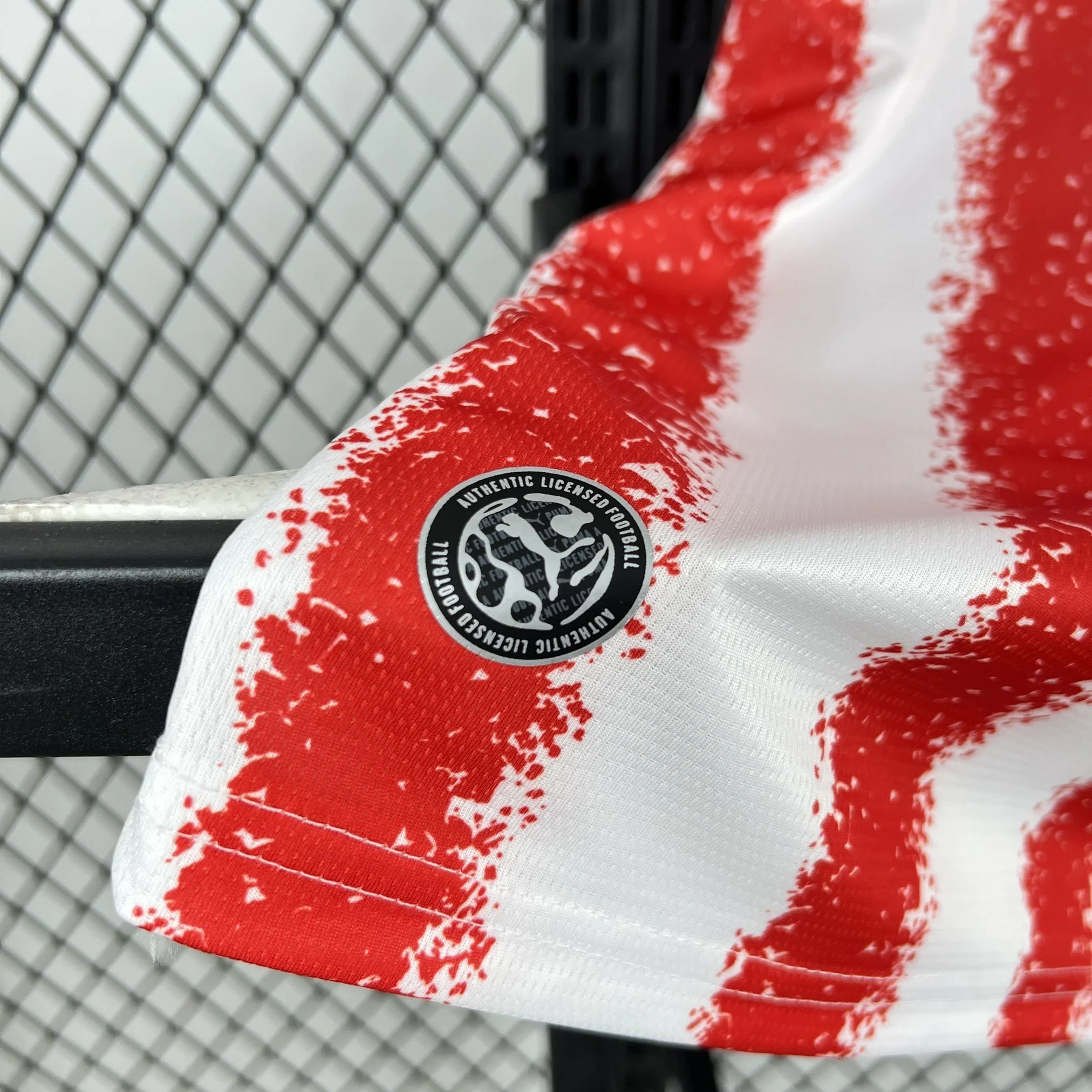 Detalle del acabado inferior de la camiseta mostrando la unión de las franjas rojas y blancas con el tejido técnico.