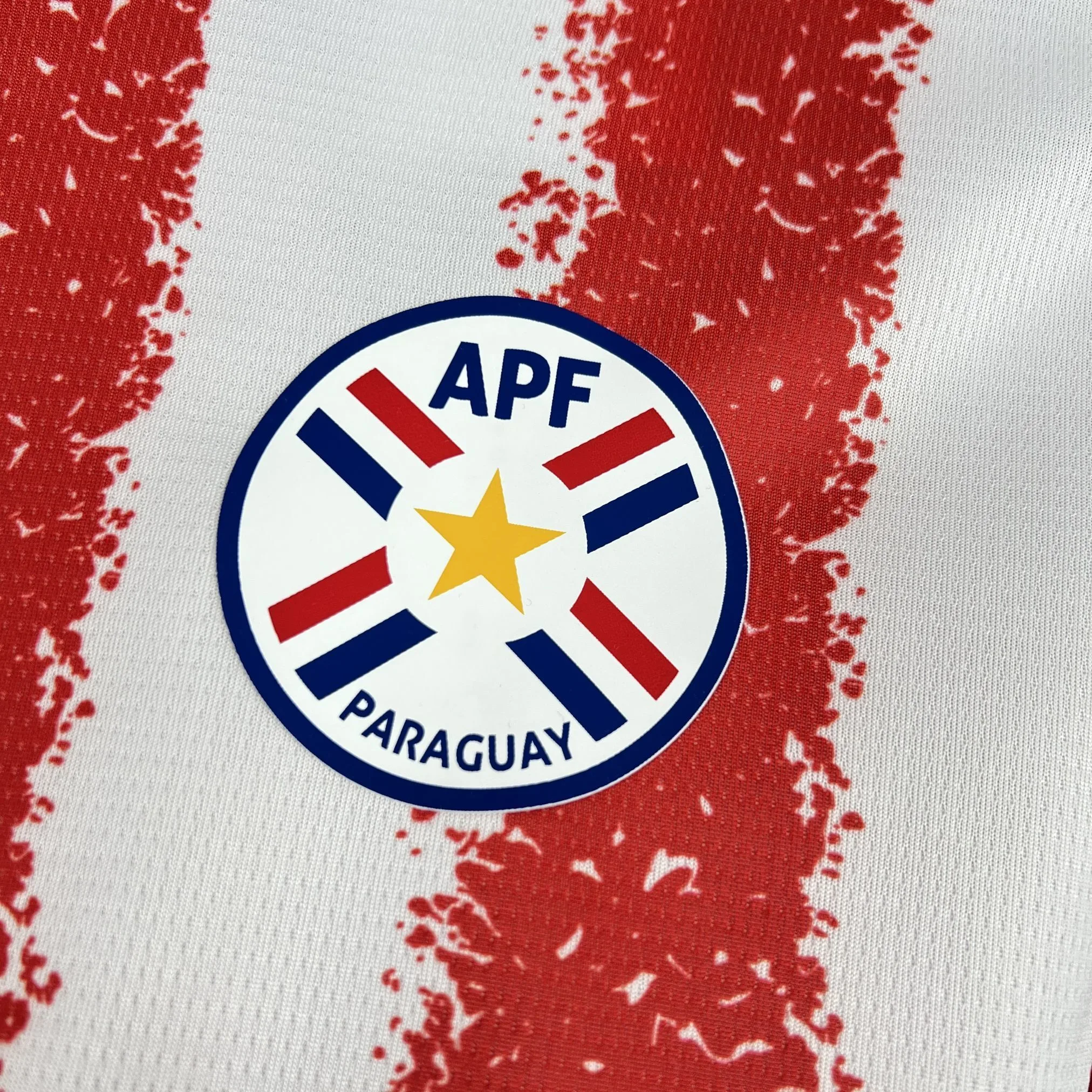 Primer plano del escudo de la Asociación Paraguaya de Fútbol con la estrella central, bordado sobre el diseño de franjas.