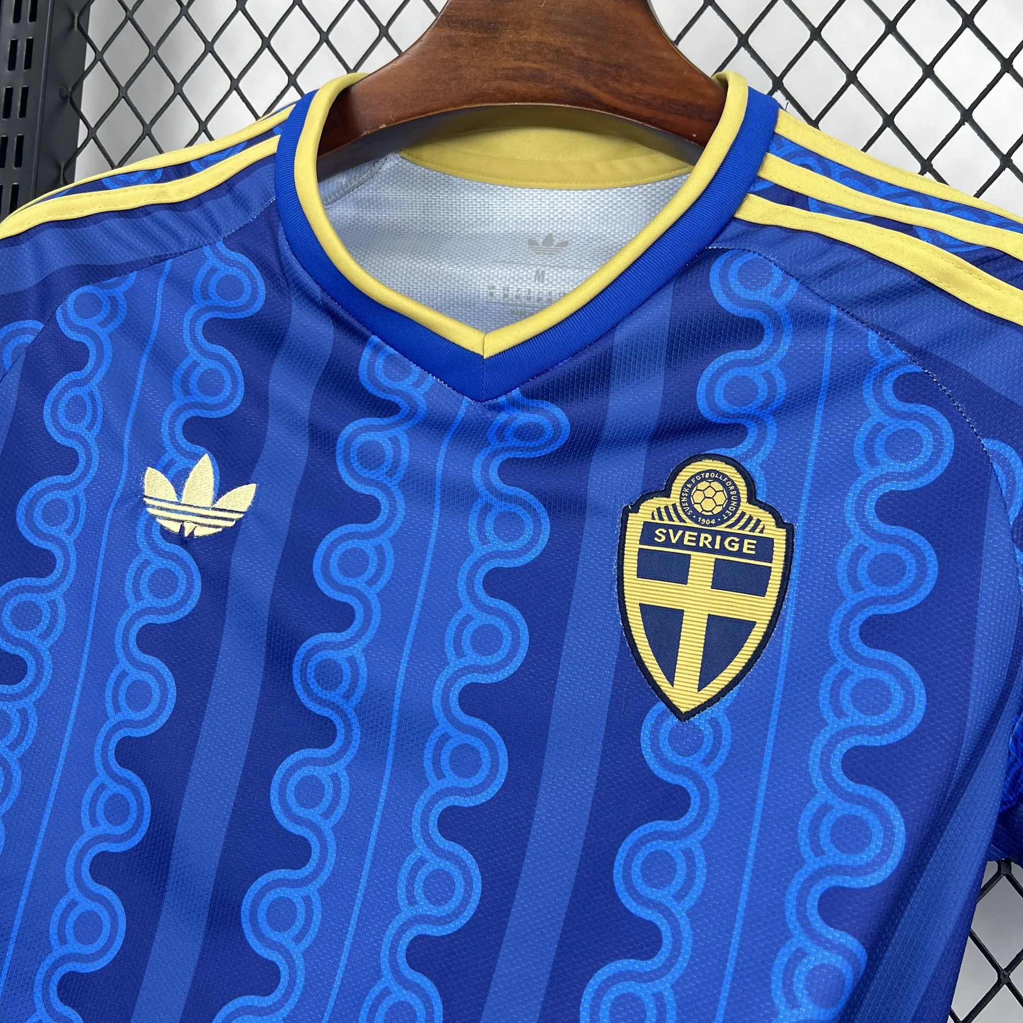 Detalle del escudo de la selección de Suecia bordado en color amarillo sobre el diseño de ondas azules.