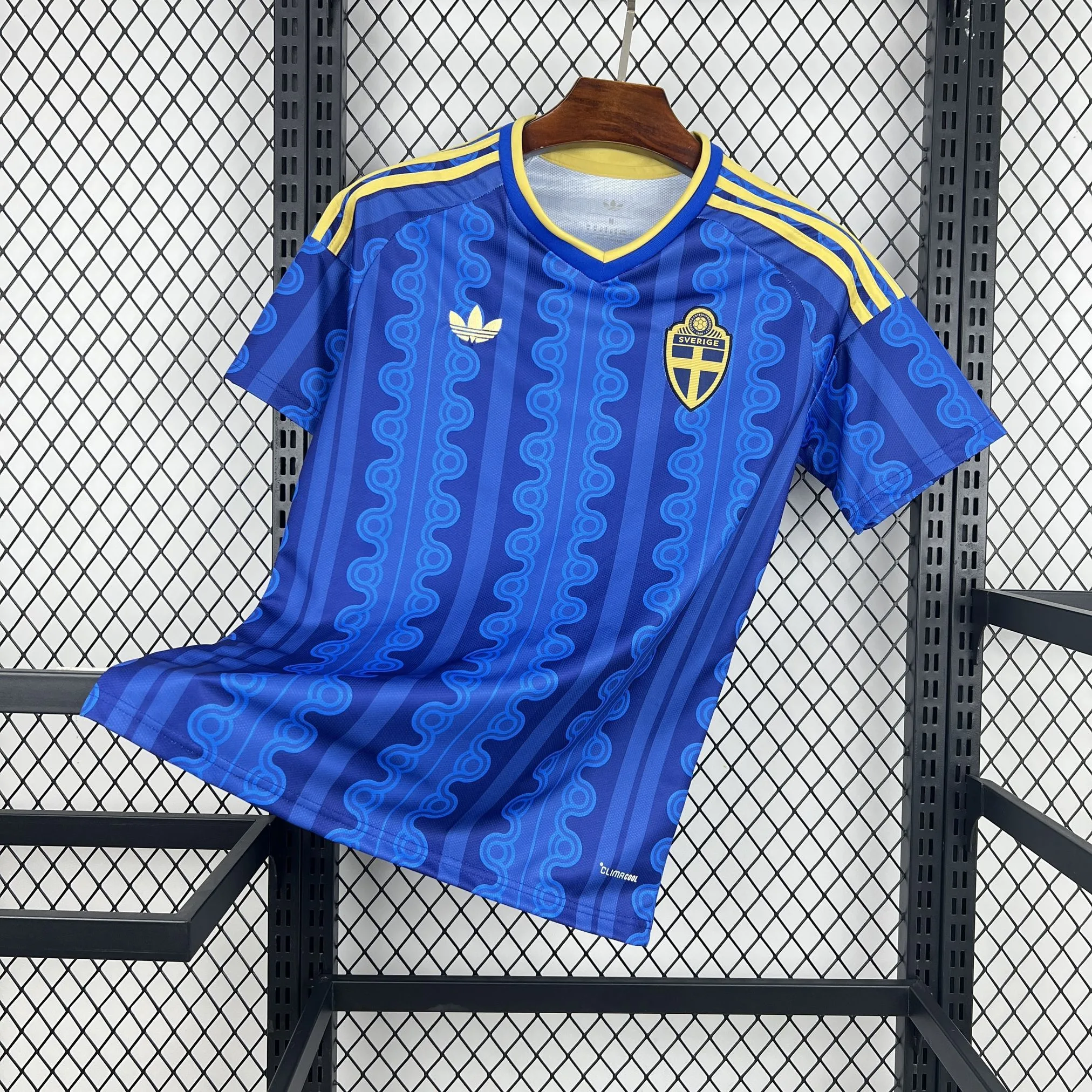 Imagen frontal completa de la camiseta visitante de Suecia, color azul marino con un diseño circular de ondas en tonos azules y rosados.