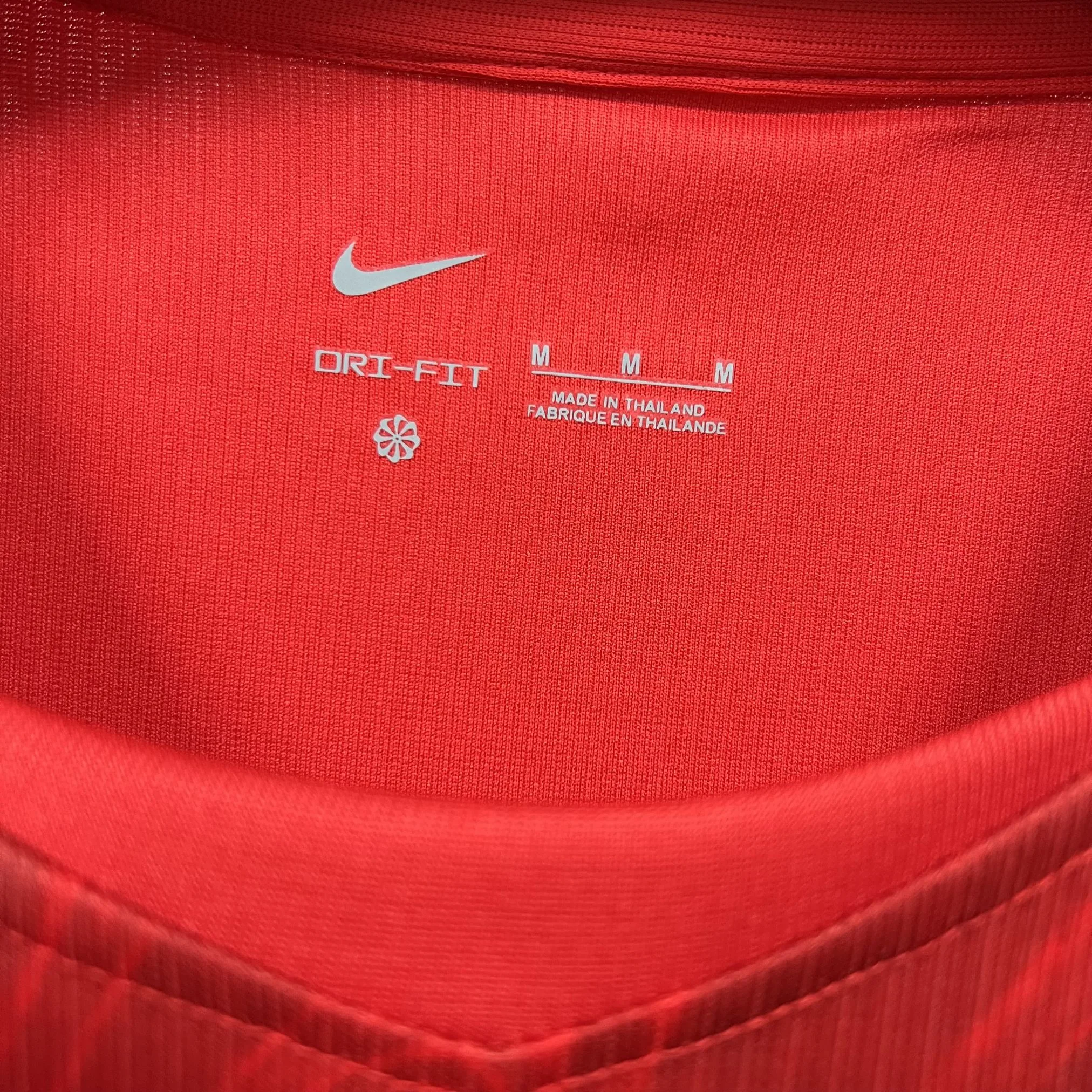 Detalle del cuello redondo rojo con ribete bicolor y gráficos técnicos impresos en el interior de la prenda.