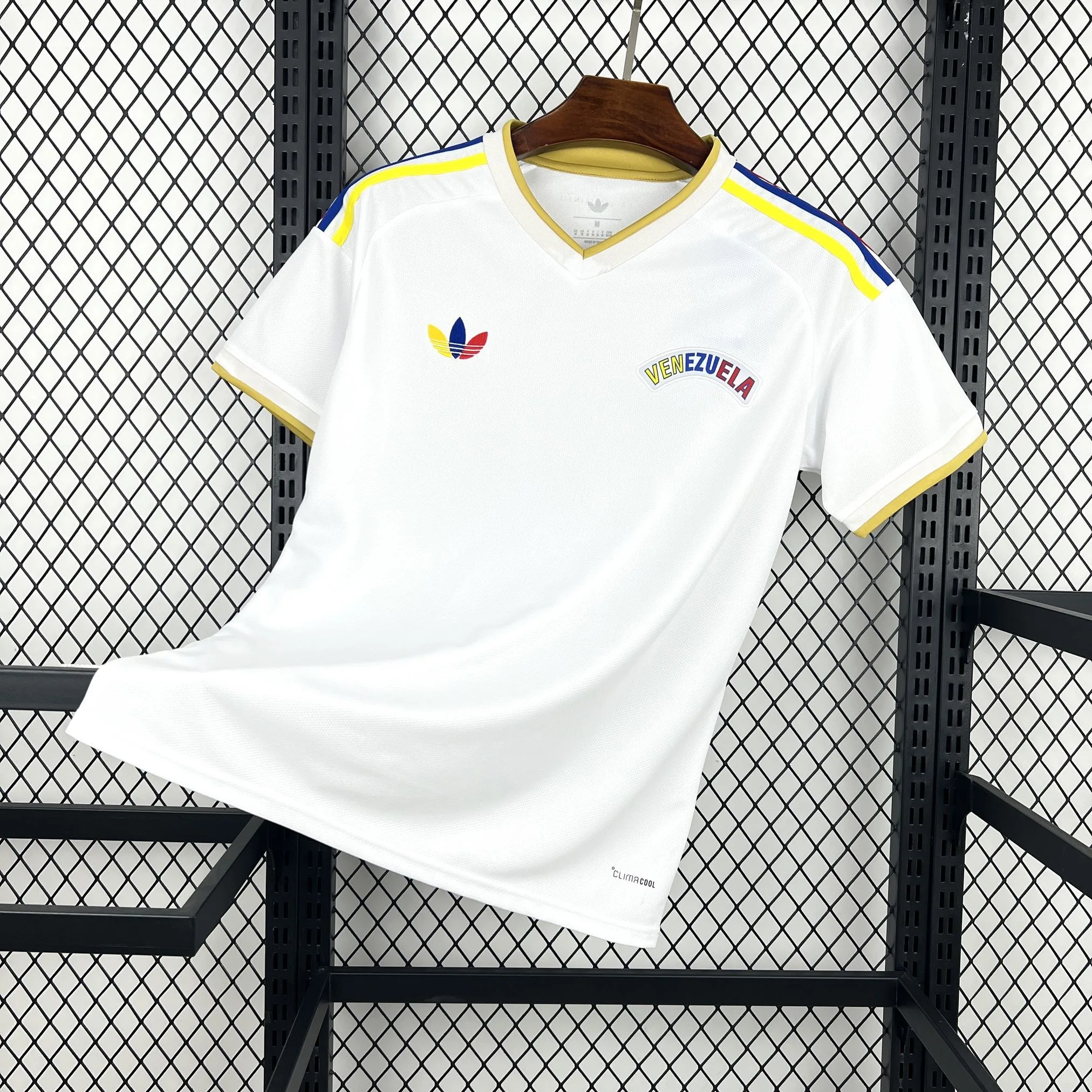 Imagen frontal completa de la camiseta visitante de Venezuela, color blanco con un gráfico central en forma de "V" en amarillo y azul.