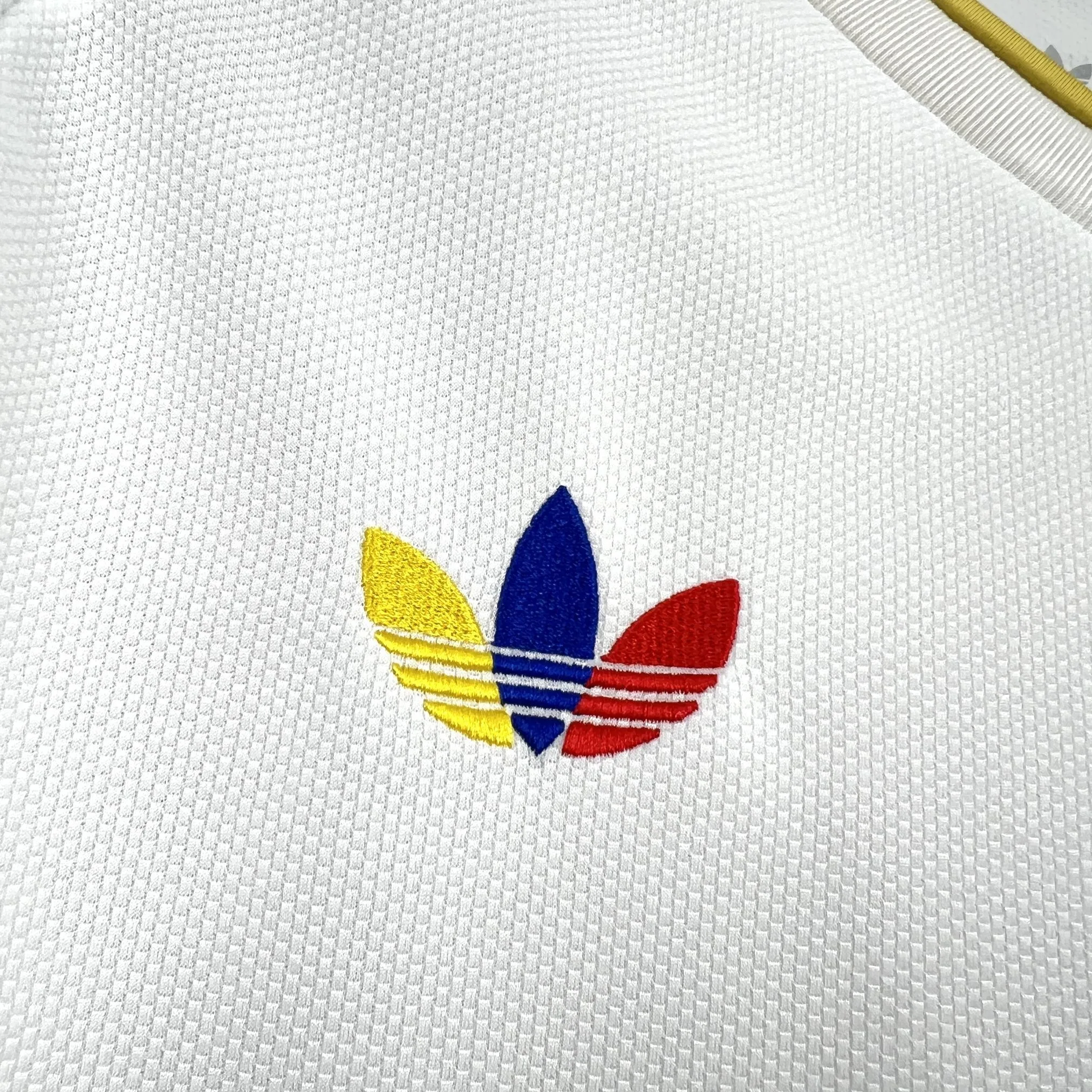 Detalle de logotipo decorativo bordado en color azul sobre el tejido técnico blanco de la prenda.
