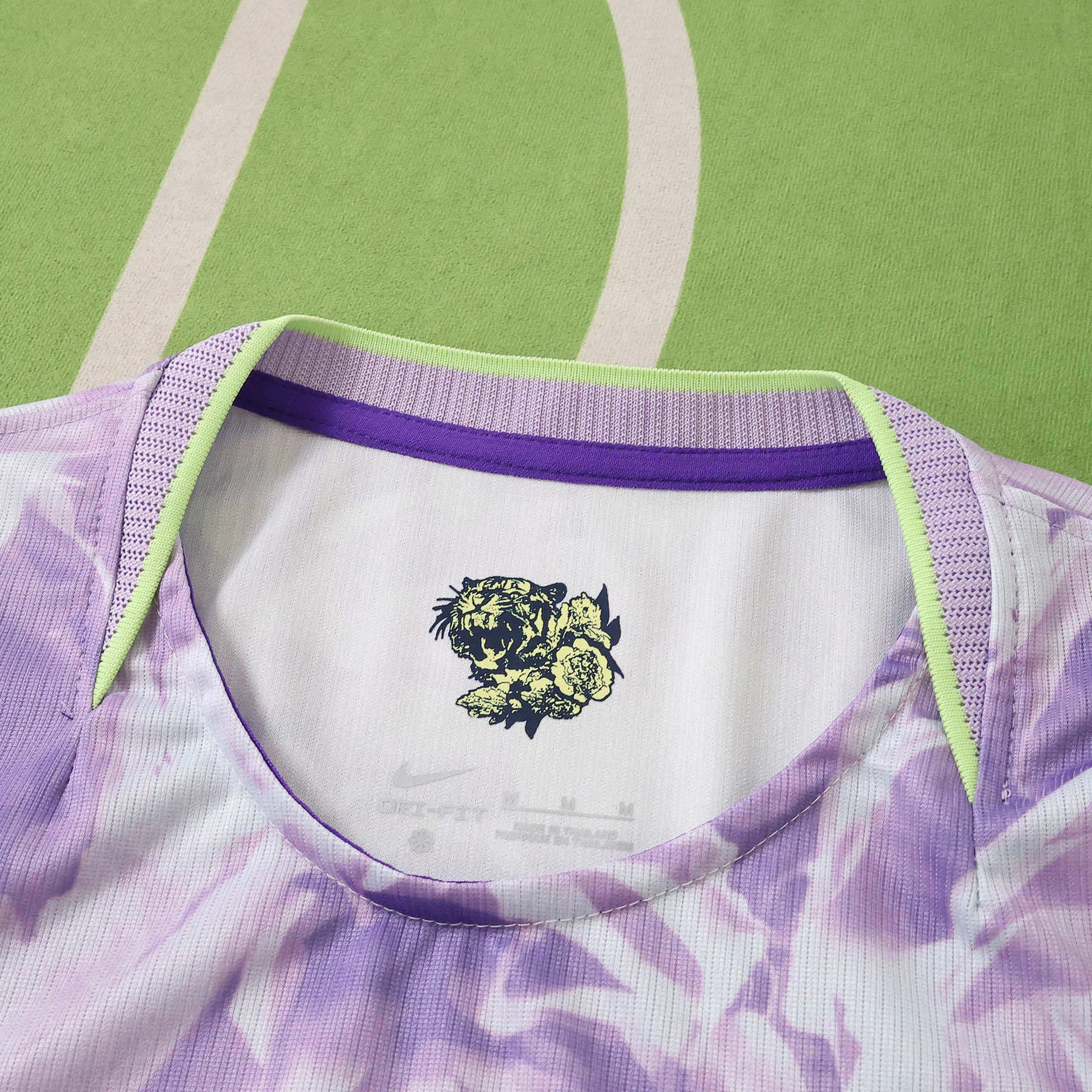 Detalle del cuello con ribete verde lima, resaltando la ilustración de un tigre negro y flores nacionales en el interior de la prenda.