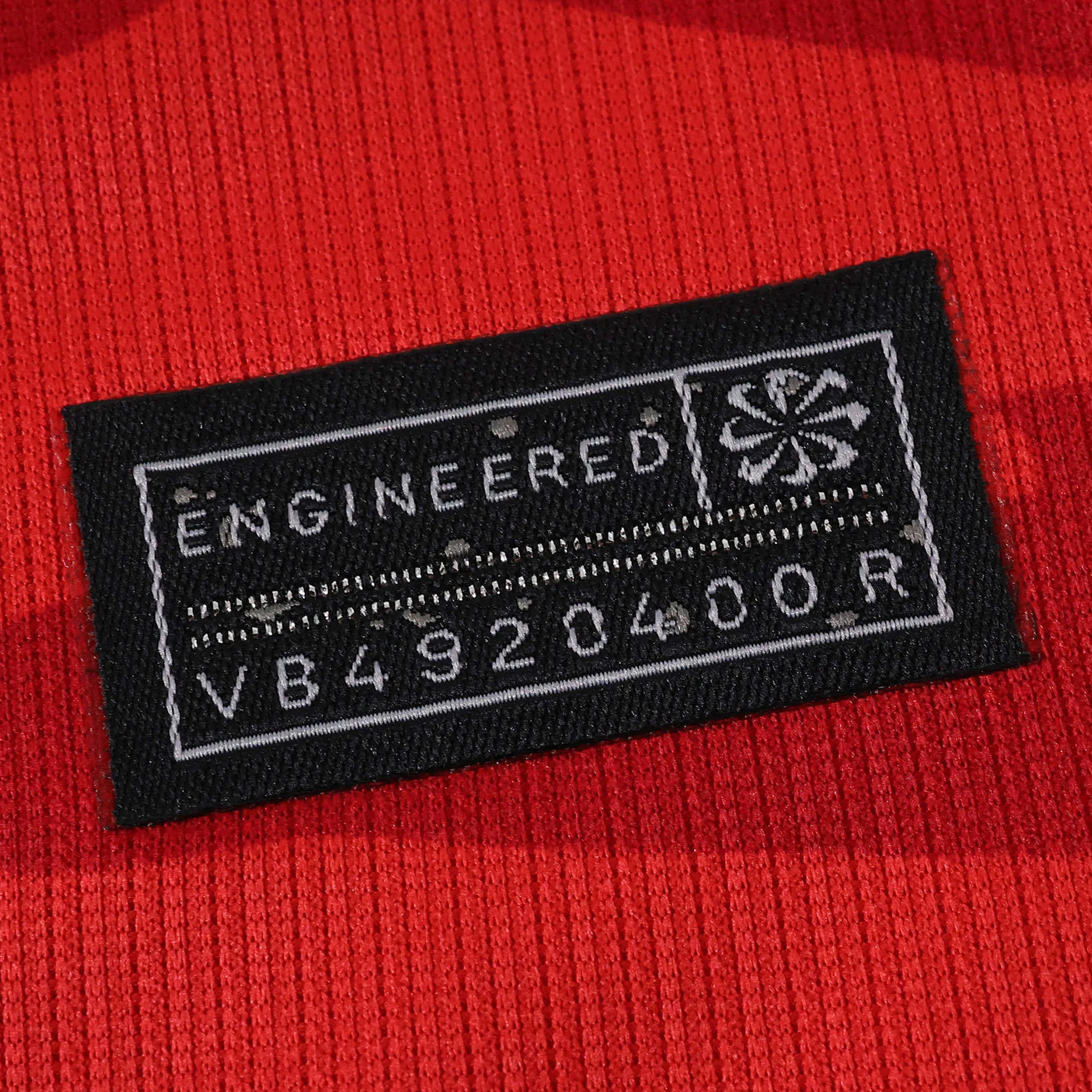 Detalle del sello rectangular de autenticidad "Engineered" en la parte inferior de la camiseta coreana.