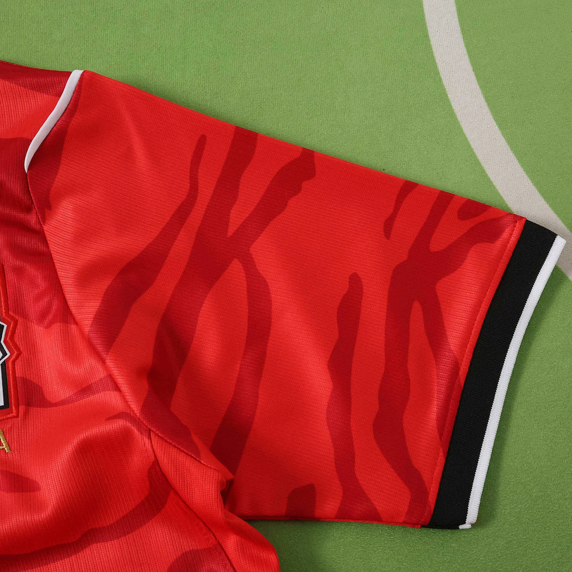 Primer plano de la manga roja con remate elástico bicolor en blanco y negro, y patrón de rayas tonales.
