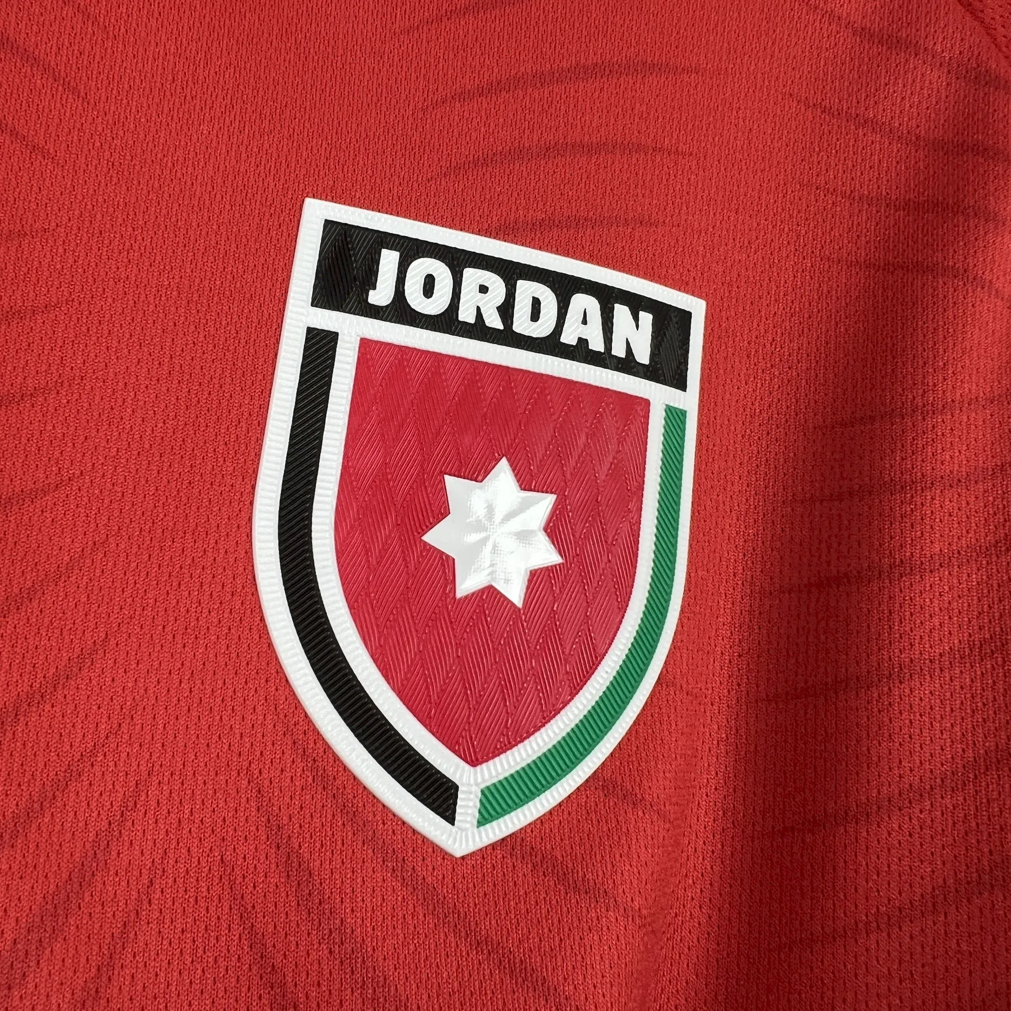 Primer plano del escudo de la Federación Jordana de Fútbol bordado sobre el tejido negro de la equipación.