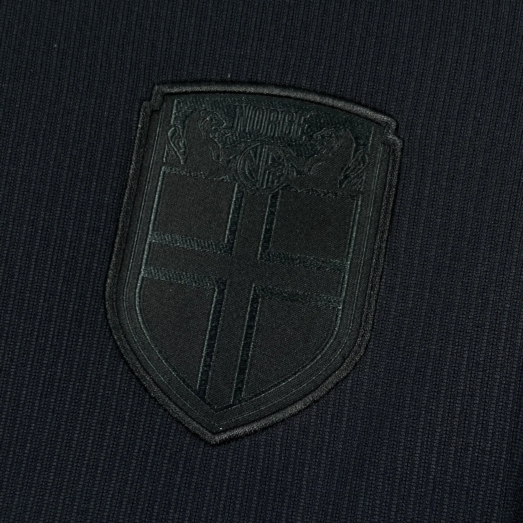 Primer plano del escudo de la selección nacional de Noruega, bordado en rojo, azul y blanco sobre el tejido texturizado.