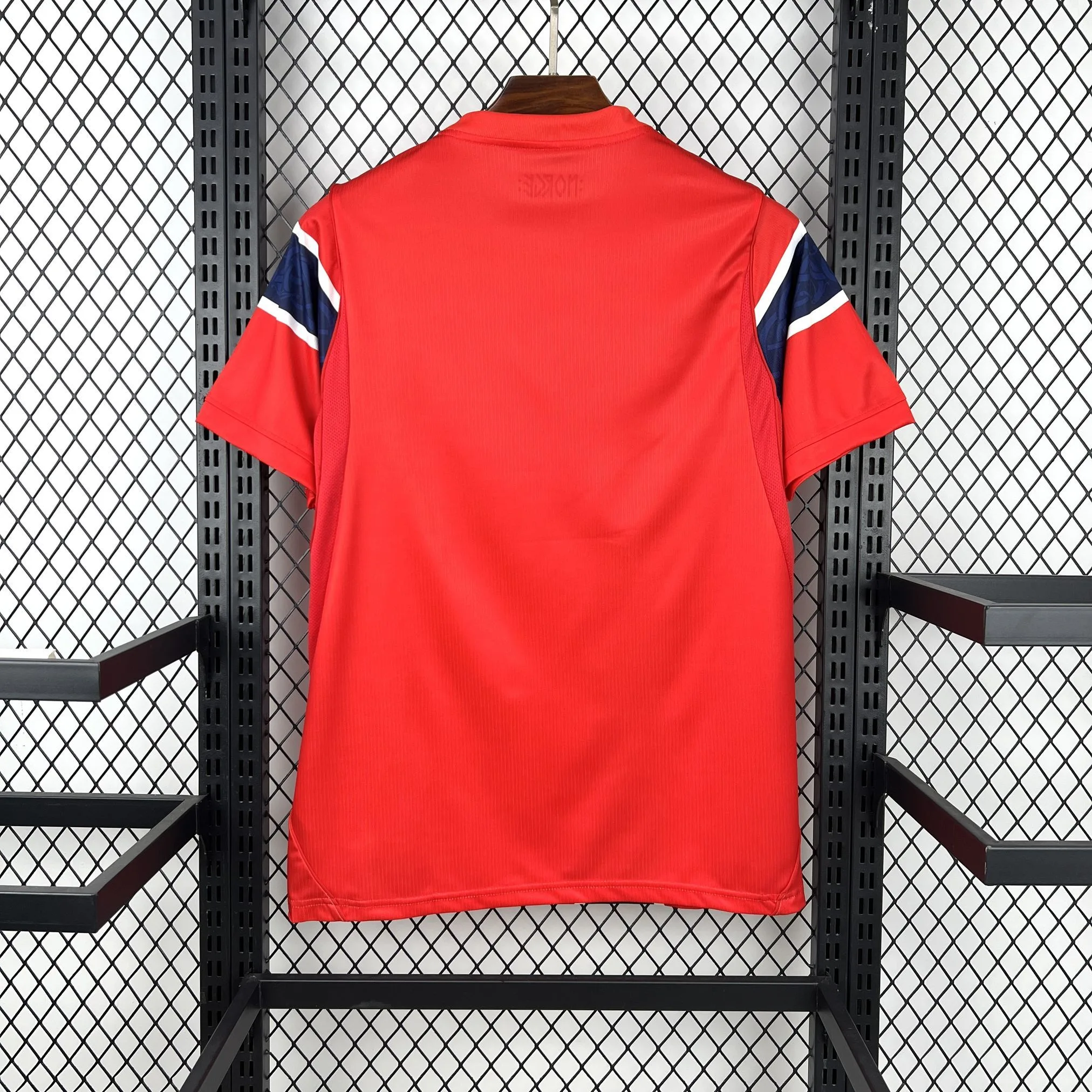 Vista posterior de la camiseta de Noruega para el Mundial 2026, diseño en rojo vibrante con una franja central vertical en azul y blanco.