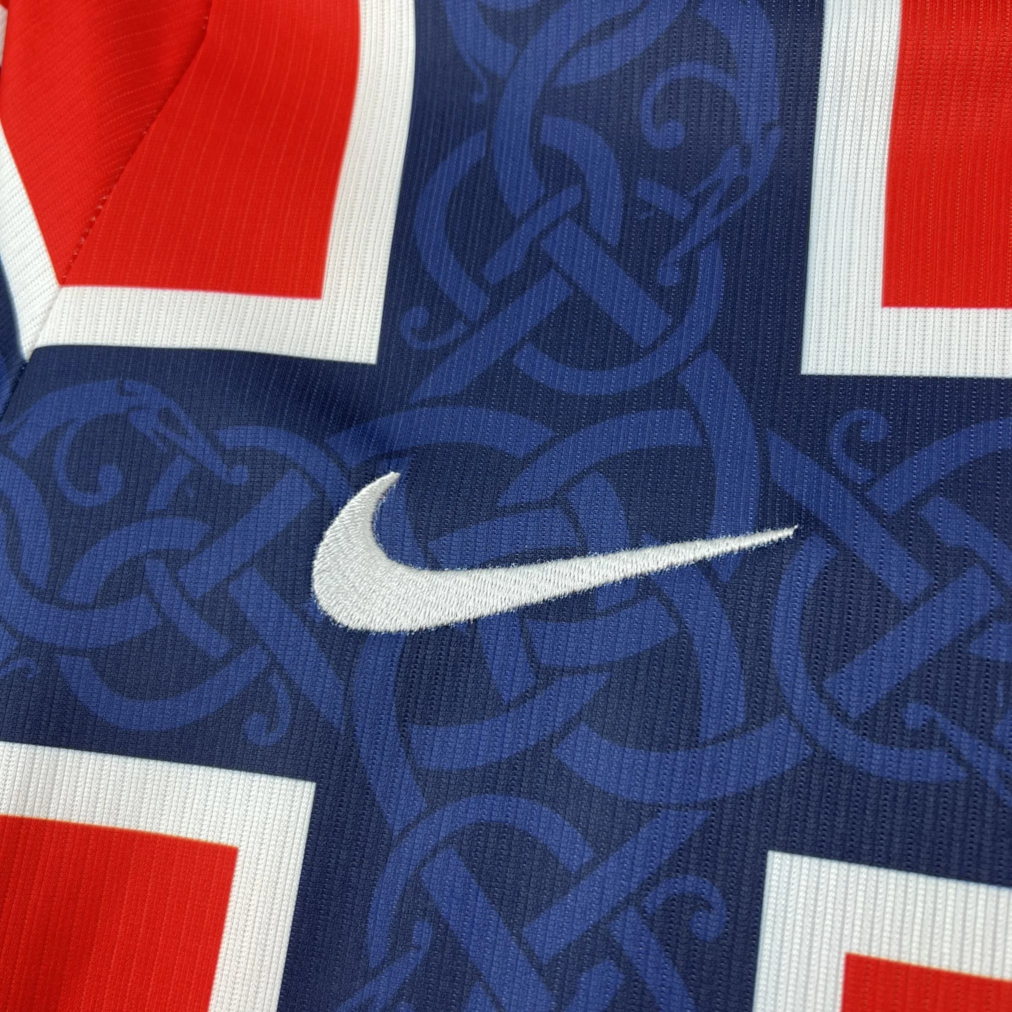 Detalle decorativo bordado en color azul marino sobre el pecho de la camiseta de Noruega.