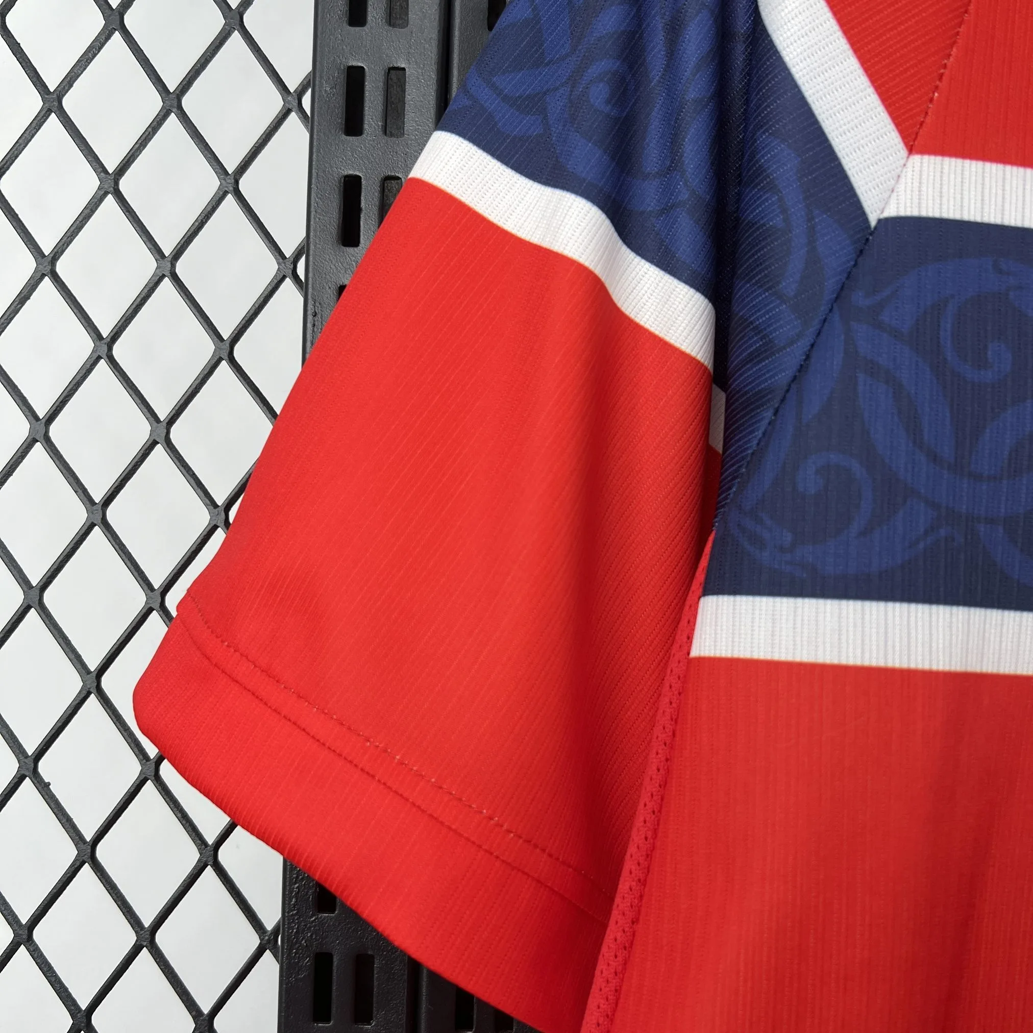 Detalle de la manga roja con remate elástico bicolor en azul y blanco, y textura de material transpirable.