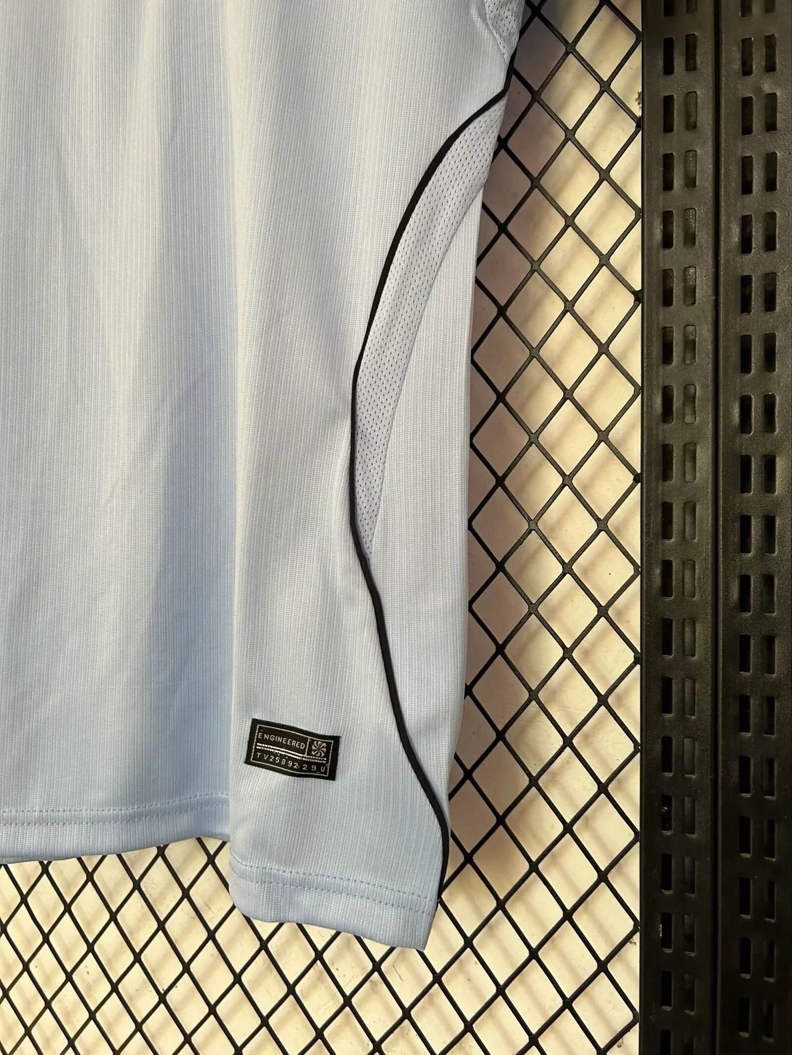 Detalle del acabado inferior de la camiseta destacando la unión del panel lateral negro y el tejido técnico celeste.